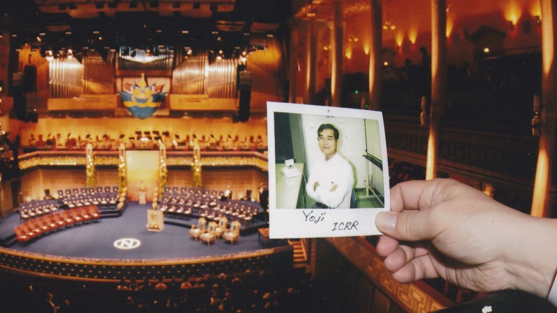 ノーベル賞授賞式の会場を背景に戸塚さんの写真