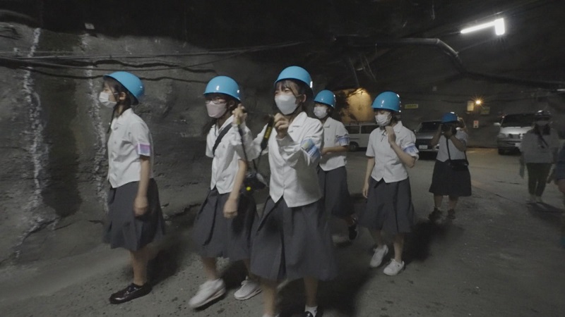 スーパーカミオカンデへ。ヘルメットをかぶりトンネルを歩く高校生たち。