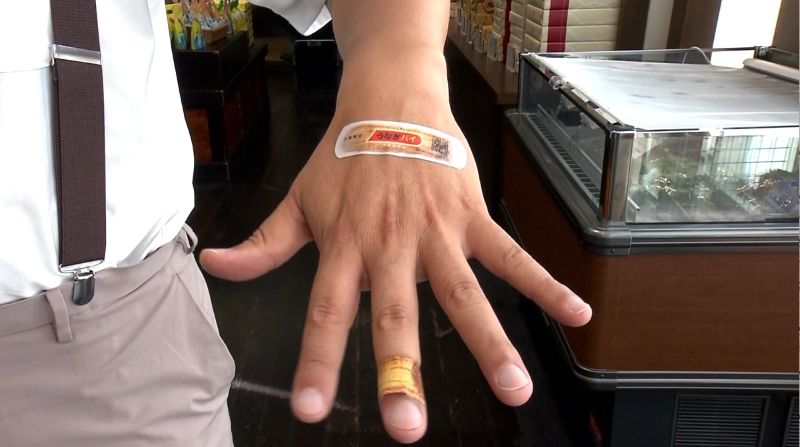 手の甲に個包装のうなぎバン　指にうなぎパイのうなぎバン