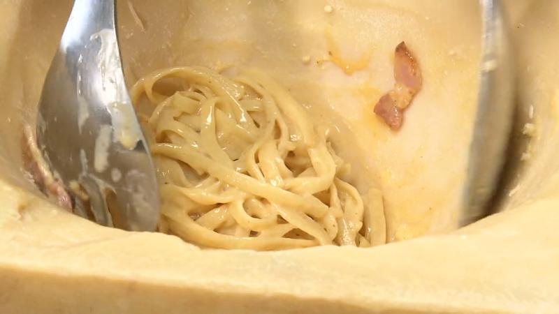 器状にしたグラナ・パダーノの中でパスタを和えている