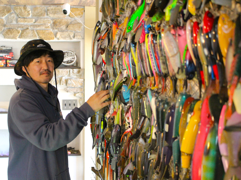オーナー・青野憲悟さんと壁に並んだルアー