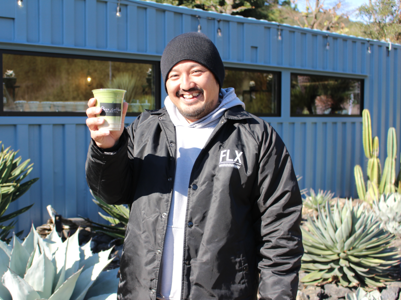 「深蒸し茶ラテ」(650円)を持つオーナーの青野巧さん