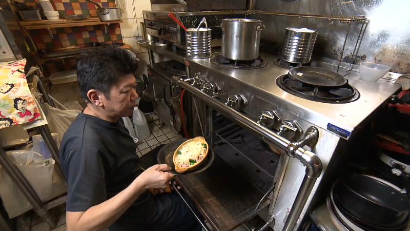 オーブンからグラタンを出す店主