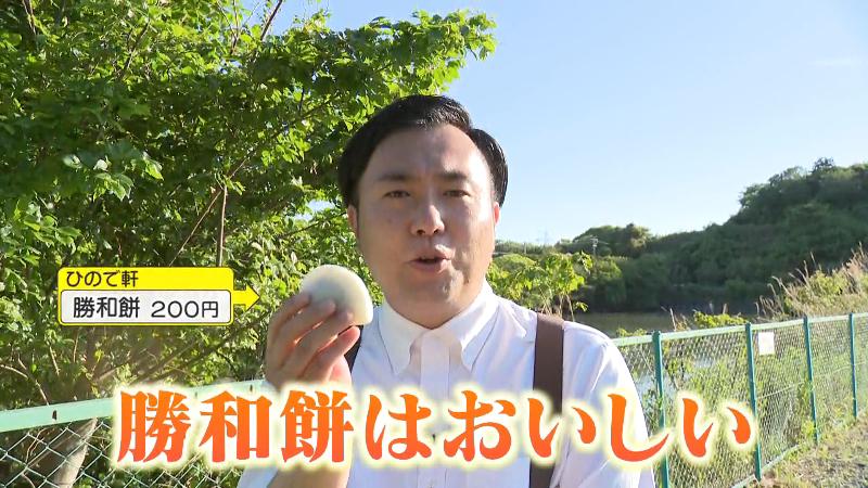 番場池を背に勝和餅を食べるにむらリポーター